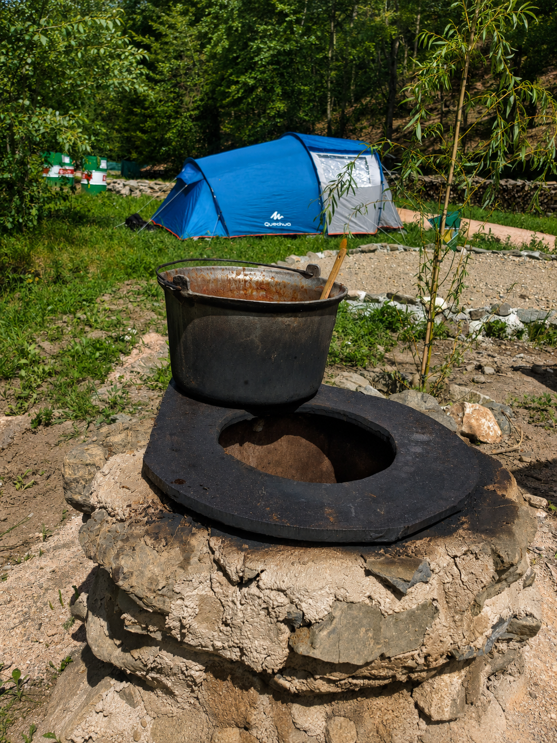 Ceaun asezat pe vatra de piatra din camping, cu un cort in fundal