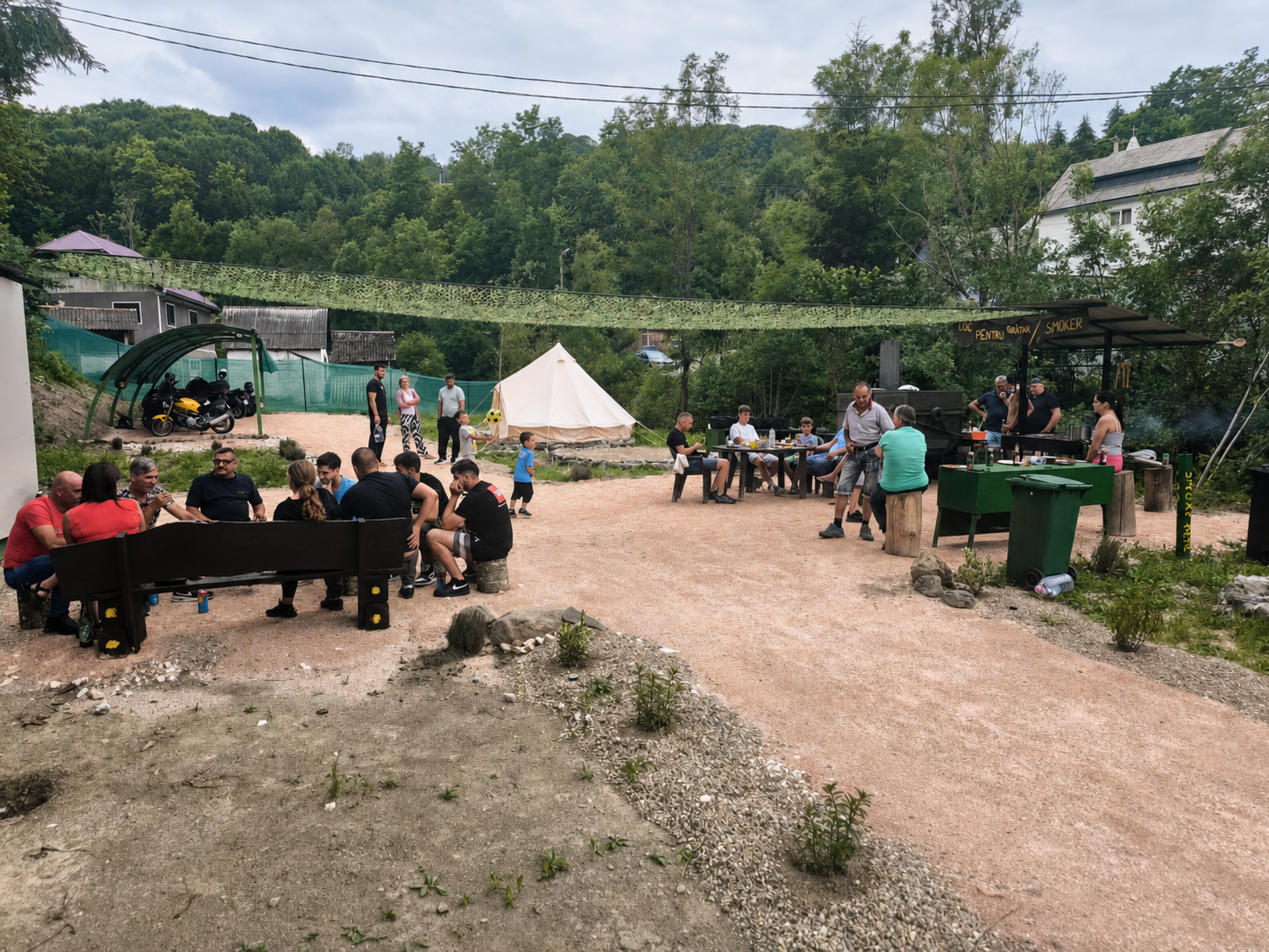 Grup de motociclisti si prieteni adunati la mesele si bancile din mijlocul campingului